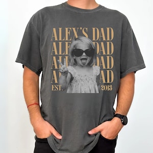 K&ouml;nnte beinhalten: Dunkelgraues T-Shirt mit einem Schwarz-Wei&szlig;-Foto eines Kindes mit Sonnenbrille und Peace-Zeichen. Der Text "ALEX'S DAD" ist &uuml;ber dem Foto aufgedruckt, darunter "EST. 2013".