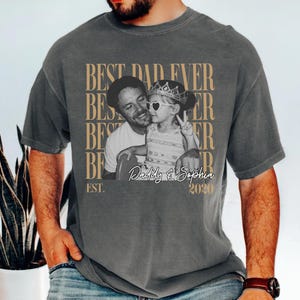 Op de afbeelding: Grijze t-shirt met een zwart-wit foto van een man en een kind. De tekst "BEST DAD EVER" staat boven de foto, met "Daddy & Sophia 2020" eronder. Het shirt heeft een casual stijl.