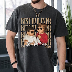 May include: Dark gray t-shirt with the text "BEST DAD EVER" repeated vertically. A photo of two children wearing sunglasses is centered below the text, with the names "Alex & Olivia" and the year "2020" below the photo.