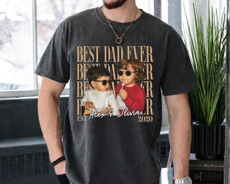 May include: Dark gray t-shirt with the text "BEST DAD EVER" repeated vertically. A photo of two children wearing sunglasses is centered below the text, with the names "Alex & Olivia" and the year "2020" below the photo.