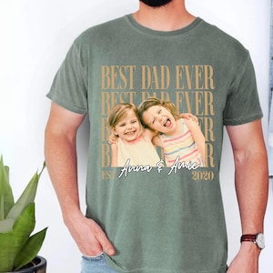 May include: Sage green t-shirt with the text "BEST DAD EVER" in a repeating pattern. The shirt features a photo of two young girls with the names "Anna & Amie" and the year "2020" printed below the photo.