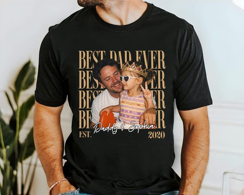 May include: Black t-shirt with a photo of a man and a child, with the text "BEST DAD EVER" repeated vertically in a gold color. The photo shows the man holding a heart-shaped object and the child wearing a crown and heart-shaped sunglasses. The text "Daddy & Sophia" and "2020" are also present.