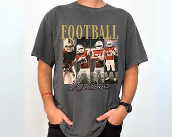May include: A charcoal gray short-sleeve t-shirt featuring the word FOOTBALL in gold letters above four vertical panels showing a football player in a red and white uniform. The name William is printed in a black script font below the panels.