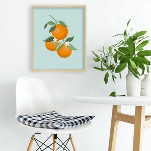 Pode incluir: Uma impress&atilde;o emoldurada de uma ilustra&ccedil;&atilde;o estilizada de tr&ecirc;s laranjas em um galho com folhas verdes e flores brancas sobre um fundo azul claro.