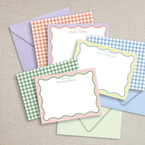 May include: A collection of personalized stationery sets featuring scalloped-edge notecards and coordinating envelopes. The notecards have a white interior and are framed with pastel colors. Gingham patterns in orange, green, and blue are visible.