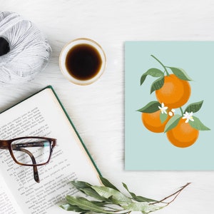 Pode incluir: Um cart&atilde;o azul claro com um gr&aacute;fico de tr&ecirc;s laranjas em um galho com folhas verdes e flores brancas. As laranjas s&atilde;o de uma cor laranja vibrante.
