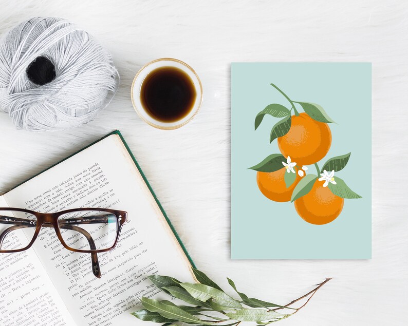 Pode incluir: Um cart&atilde;o azul claro com um gr&aacute;fico de tr&ecirc;s laranjas em um galho com folhas verdes e flores brancas. As laranjas s&atilde;o de uma cor laranja vibrante.
