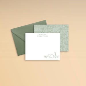 Puede incluir: Una tarjeta de agradecimiento blanca con un sobre verde. La tarjeta presenta un dibujo lineal de un elefante, una jirafa y dos animales m&aacute;s peque&ntilde;os. El texto "Thank you from EVERETT JUDSON" est&aacute; impreso en la tarjeta.