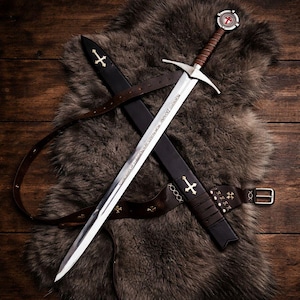 May include: A medieval sword with a silver blade and a brown leather-wrapped handle, resting on a fur rug. The sword is in a black leather sheath with a brown leather belt. The hilt features a red and white emblem.
