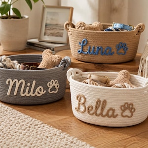 Peut inclure: Trois paniers en corde tress&eacute;e pour animaux de compagnie, chacun avec un nom et une empreinte de patte. Le panier gris dit "Milo", le panier beige dit "Luna", et le panier blanc dit "Bella". Chaque panier contient des fournitures pour animaux.