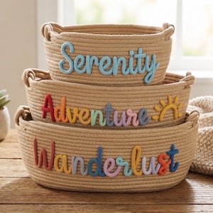 Peut inclure: Trois paniers en corde tress&eacute;e empil&eacute;s sur une surface en bois. Le panier sup&eacute;rieur porte le mot "Serenity" en lettres bleu clair. Le panier du milieu porte "Adventure" en lettres color&eacute;es, et le panier inf&eacute;rieur porte "Wanderlust" en lettres color&eacute;es.