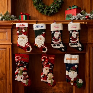 Op de afbeelding: Een verzameling gepersonaliseerde kerstsokken, elk met een naam geborduurd op de manchet. De sokken hebben feestelijke ontwerpen, waaronder de kerstman, sneeuwpoppen en zuurstokken, met een verscheidenheid aan kleuren.