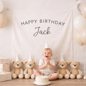 Può includere: Scena del primo compleanno con uno striscione che recita "Happy Birthday Jack". L'immagine include palloncini, orsacchiotti, regali e una piccola torta con una singola candela. Il bambino indossa un cappello da festa e sorride.