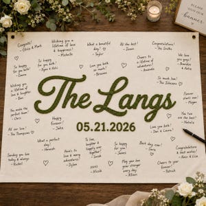 May include: A rectangular off-white fabric guest book banner featuring the embroidered dark green text The Langs and the date 05.21.2026. The banner is filled with handwritten congratulatory messages and small heart doodles in black ink.