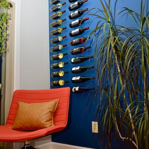 May include: A wall mounted wine rack with 18 bottles of wine, a red chair with a brown pillow, and a green plant in a white and black patterned pot.