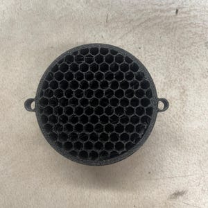 Puede incluir: Rejilla redonda de altavoz negra con un patrón de panal.