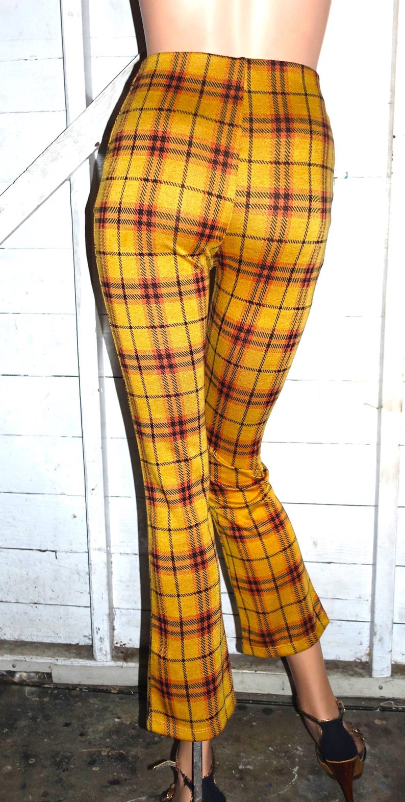 Puede incluir: Pantal&oacute;n acampanado de cuadros amarillos, negros y naranjas. El pantal&oacute;n est&aacute; hecho de una tela el&aacute;stica y tiene una silueta ajustada.