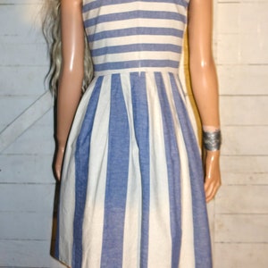 Może przedstawiać: Biało-niebieska, bezrękawowa sukienka z dekoltem w kształcie litery V. Sukienka ma plisowaną sp&oacute;dnicę i dopasowany gorset.