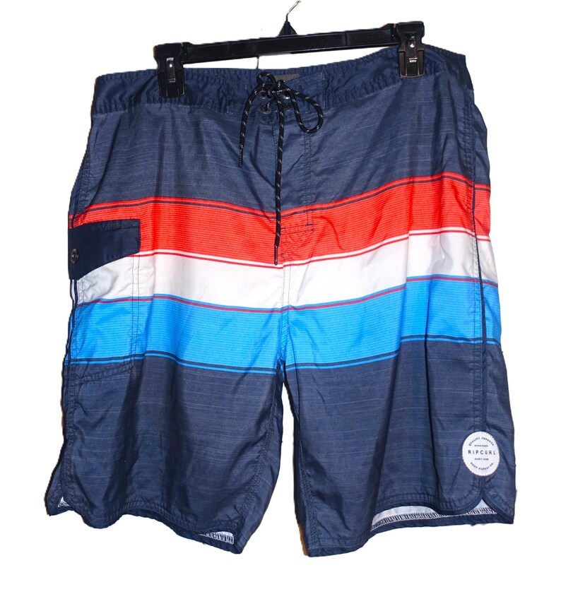 May include: Blue, red, and white striped swim trunks with a black Rip Curl logo on the right leg.