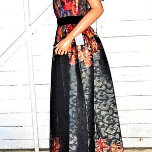 Puede incluir: Un vestido maxi negro y dorado con estampado floral. El vestido tiene un corpi&ntilde;o ajustado y una falda fluida. El estampado floral es en tonos de rojo, naranja, amarillo y azul.