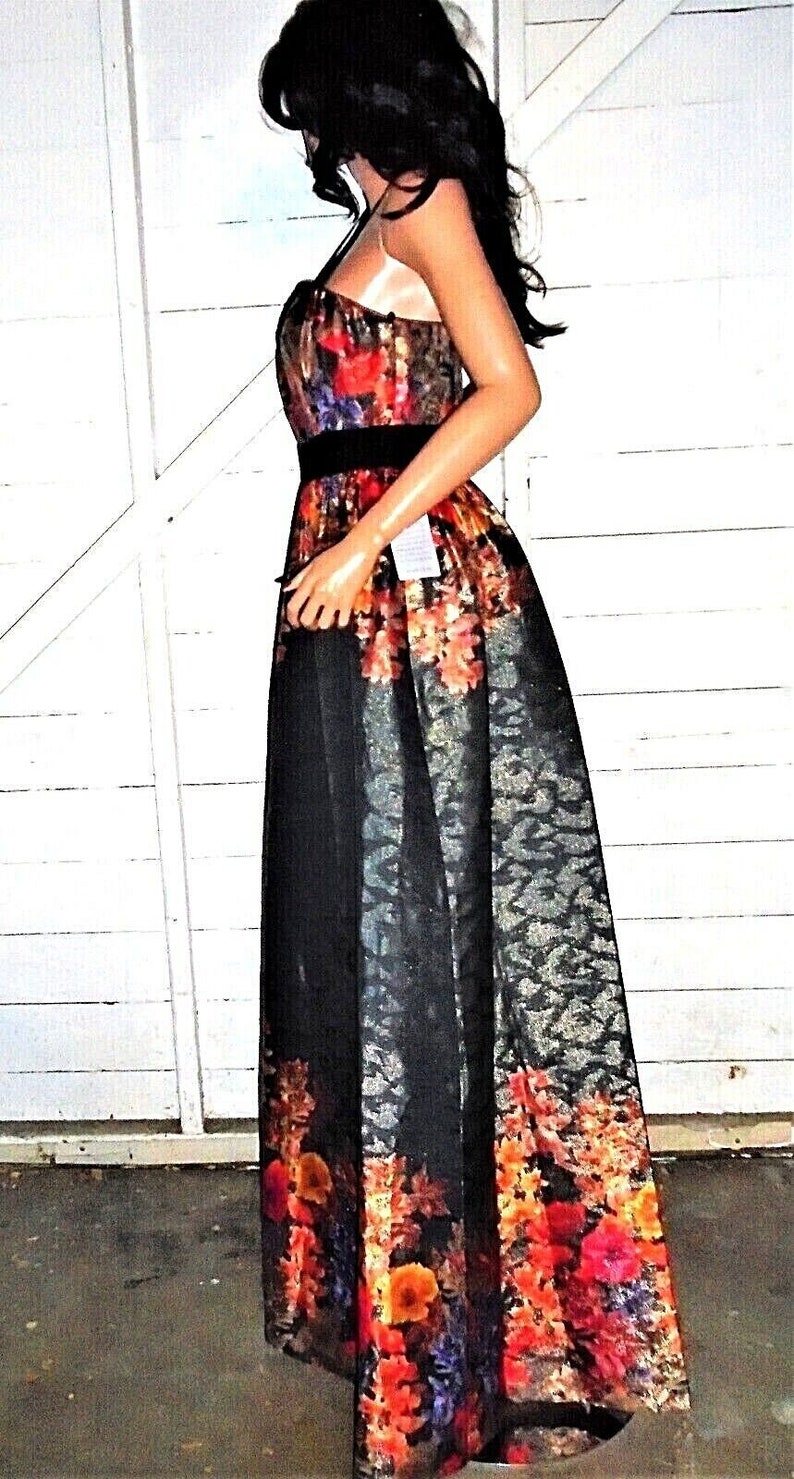 Puede incluir: Un vestido maxi negro y dorado con estampado floral. El vestido tiene un corpi&ntilde;o ajustado y una falda fluida. El estampado floral es en tonos de rojo, naranja, amarillo y azul.
