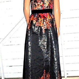 Puede incluir: Un vestido maxi negro con estampado floral. El vestido tiene un corpi&ntilde;o ajustado y una falda fluida. El estampado floral es en tonos de rojo, naranja, amarillo y azul.