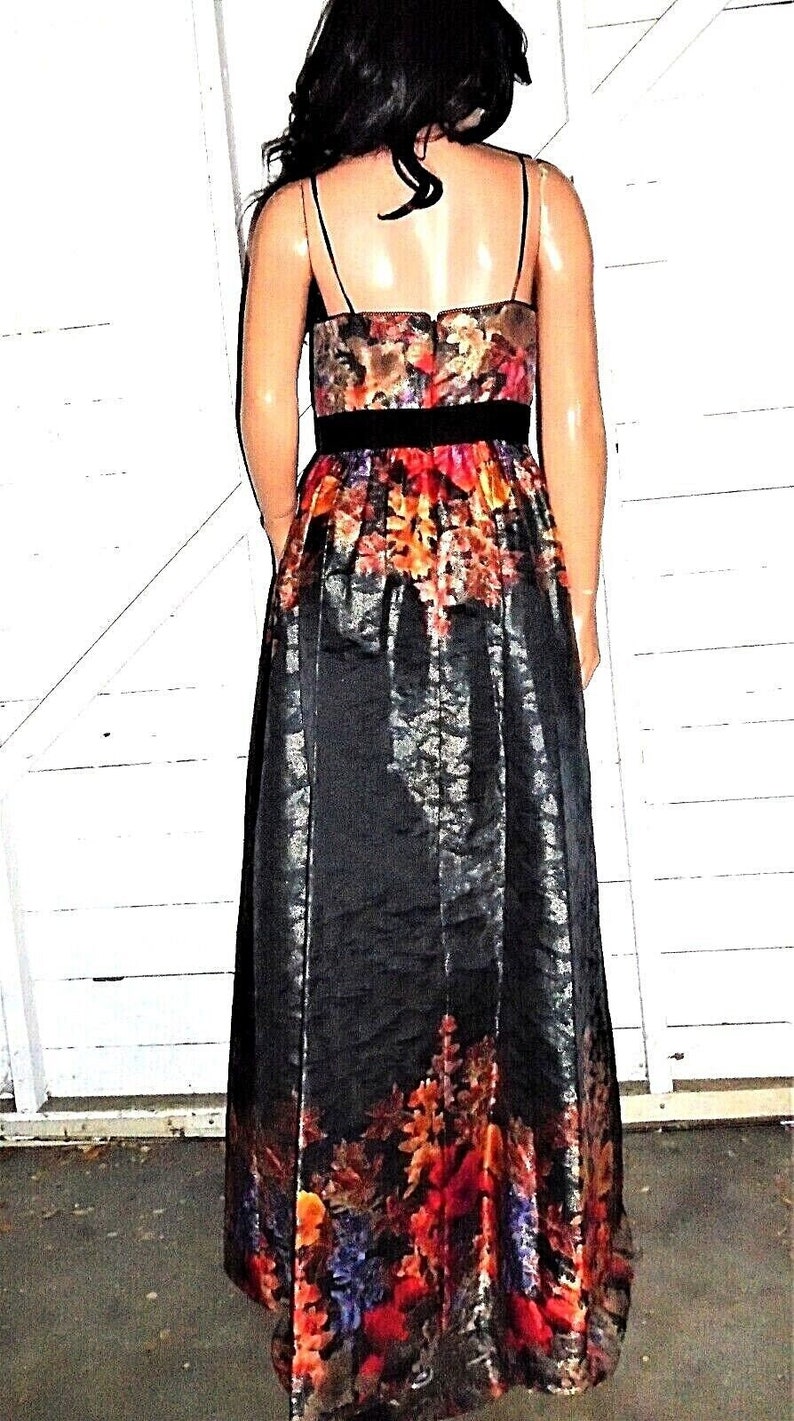 Puede incluir: Un vestido maxi negro con estampado floral. El vestido tiene un corpi&ntilde;o ajustado y una falda fluida. El estampado floral es en tonos de rojo, naranja, amarillo y azul.