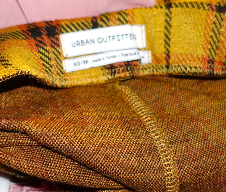 Puede incluir: Tela de cuadros amarilla y naranja con una etiqueta blanca que dice "URBAN OUTFITTER" y "XS-TP".