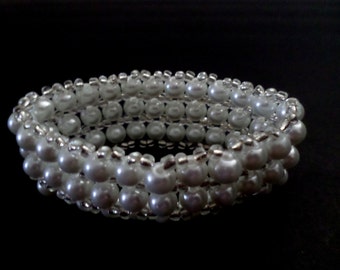 May include: A white pearl bracelet with multiple strands. The bracelet is made of small, round, white pearls and silver-coloured beads. The bracelet is on a black background.