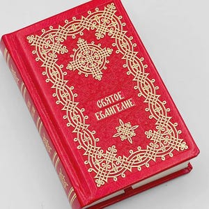 May include: A red book with gold embossed decorative patterns and the text "Святое Евангелие". The book has gold gilded edges and a matching spine. The cover features an ornate cross design.