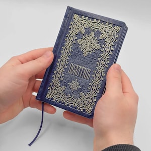 May include: A navy blue book with gold embossed decorative patterns and text. The book has a matching blue ribbon bookmark. The cover features an ornate design with a central cross and the word "Псалтирь".
