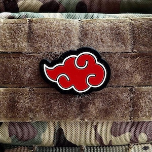 May include: A red cloud-shaped patch with a white outline and black border, attached to camouflage fabric. The patch features a stylized cloud design, often seen in anime and manga.