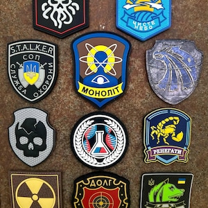 May include: A selection of embroidered patches with diverse designs. The patches display images like a skull, a scorpion, a nuclear symbol, and Cyrillic text. The patches come in various shapes, including shields and squares, and feature a range of colours.