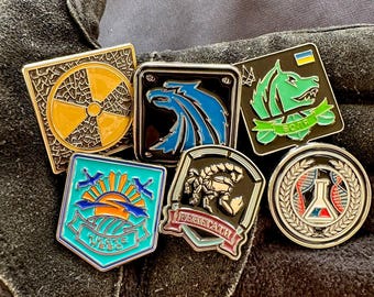 May include: A collection of enamel pins featuring various designs, including a nuclear symbol, a wolf, a scorpion, a sunrise, a wolf head, and a chemical symbol. The pins are all silver-toned with colorful accents.