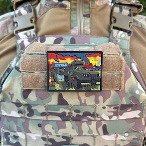 Może przedstawiać: Prostokątna naszywka z kolorową ilustracją pojazdów wojskowych i żołnierzy, z białym napisem "КУРСК". Naszywka jest umieszczona na tle kamuflażu i jest przymocowana do kamizelki taktycznej.