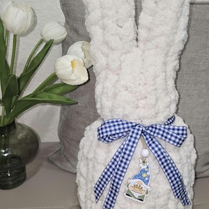 May include: A white crocheted bunny rabbit with a blue and white gingham ribbon bow. The bunny has a small wooden gnome ornament hanging from the bow.
