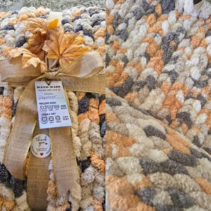 Puede incluir: Una manta de punto grueso con un patr&oacute;n variado de hilo color crema, melocot&oacute;n y gris carb&oacute;n. La manta est&aacute; atada con una cinta de arpillera color canela, decorada con hojas de oto&ntilde;o artificiales y una etiqueta que dice HAND MADE.
