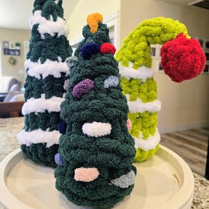 Puede incluir: Tres adornos navideños hechos a mano con forma de árbol. Los árboles están hechos de hilo verde, blanco y amarillo. Un árbol es verde oscuro con detalles blancos, otro es verde con adornos coloridos y el tercero es verde lima con una bola roja.