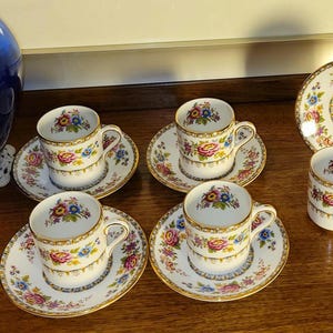 May include: Five floral teacups and saucers with gold trim. The cups and saucers have a white background with a colorful floral pattern.