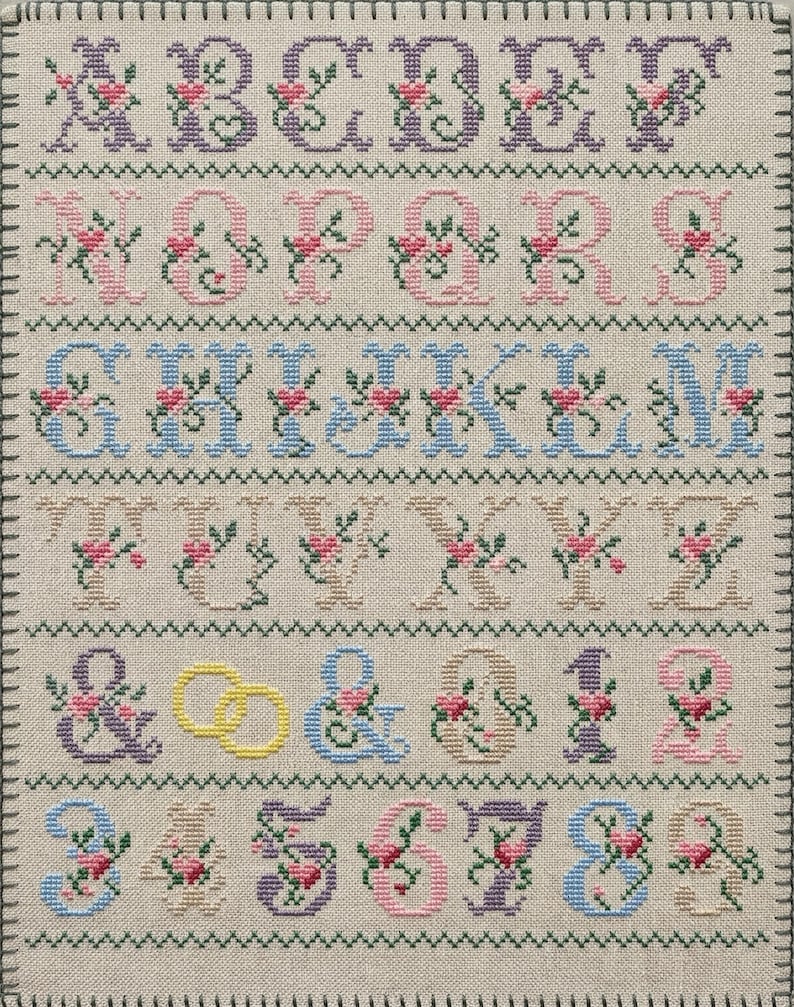 Elegant wedding alphabet cross stitch pattern with floral letters A–Z, digits 0–9, ampersand, hearts, and rings in pastel colors on grid chart for digital PDF download