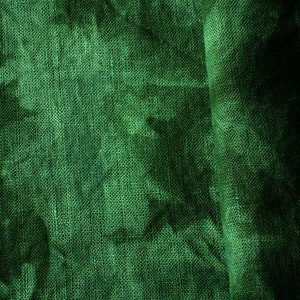 May include: Close-up of a textured, emerald green fabric. The fabric has a woven appearance with visible threads and a slight sheen. The folds create shadows, adding depth to the material. The overall effect is a rich, luxurious textile.