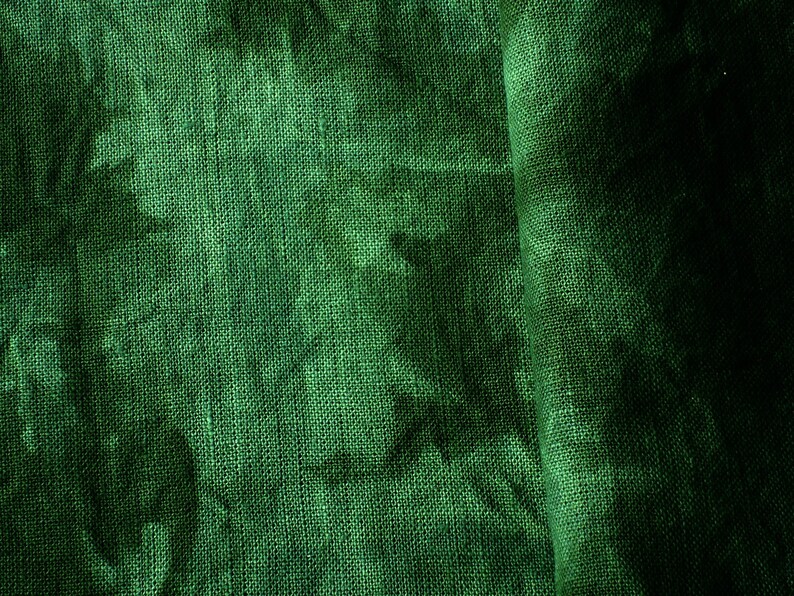 May include: Close-up of a textured, emerald green fabric. The fabric has a woven appearance with visible threads and a slight sheen. The folds create shadows, adding depth to the material. The overall effect is a rich, luxurious textile.