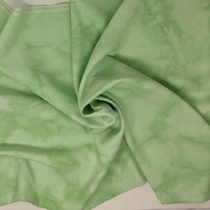 May include: A light green fabric with a tie-dye pattern. The fabric is soft and has a smooth texture.