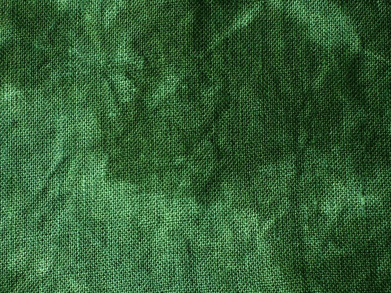 May include: Close-up of a textured, green fabric. The material has a woven appearance with visible fibers, creating a rough, uneven surface. The color is a deep, rich green, with variations in tone across the fabric.