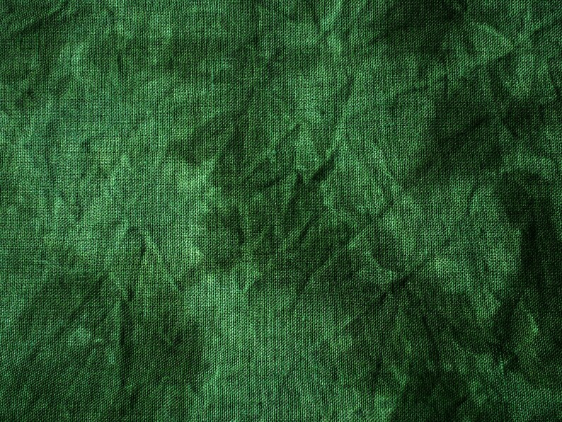 May include: Close-up of a textured, emerald green fabric. The material has a crinkled appearance, with shadows and highlights creating depth. The weave of the fabric is visible, adding to the tactile quality of the image. The overall effect is a rich, deep green.