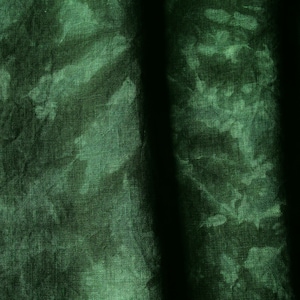 May include: Close-up of a dark green fabric with a tie-dye effect. The fabric has a textured appearance with lighter green patches against a darker green background. Vertical shadows create depth.