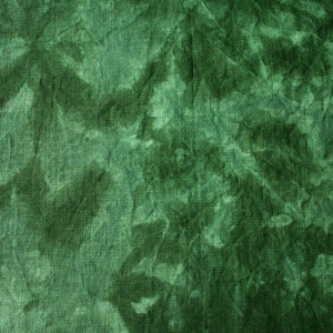 May include: Close-up of a textured fabric in shades of green. The fabric has a crinkled appearance with darker areas creating a mottled effect. The overall look is reminiscent of tie-dye or a watercolor painting.