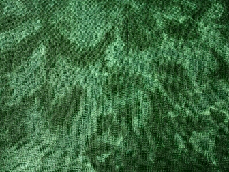 May include: Close-up of a textured fabric in shades of green. The fabric has a crinkled appearance with darker areas creating a mottled effect. The overall look is reminiscent of tie-dye or a watercolor painting.