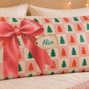 May include: A rectangular pillowcase featuring a repeating checkered pattern of light pink squares and white squares, each containing a small green or orange Christmas tree. A large pink bow is centered with a gift tag labeled with the name Alice.