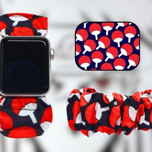 Può includere: Un cinturino per Apple Watch con motivo rosso, bianco e nero con un simbolo rosso e bianco. Il cinturino è in tessuto e ha un design a scrunchie.